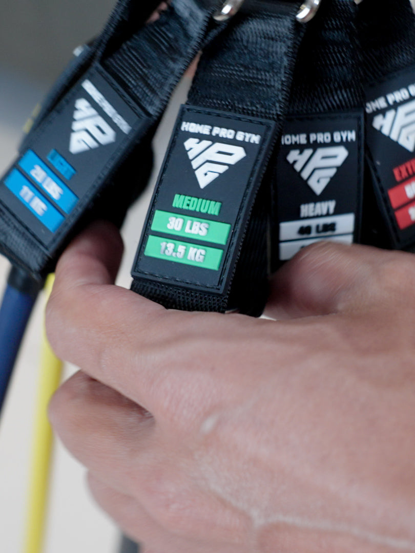 Man training at home with HomeProGym stackable resistance bands, performing chest press and squat with bands stacked for heavy resistance