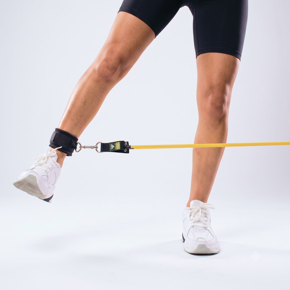 Standing glute kickback with an Ankle Strap, band clipped to the D-ring and anchored low.