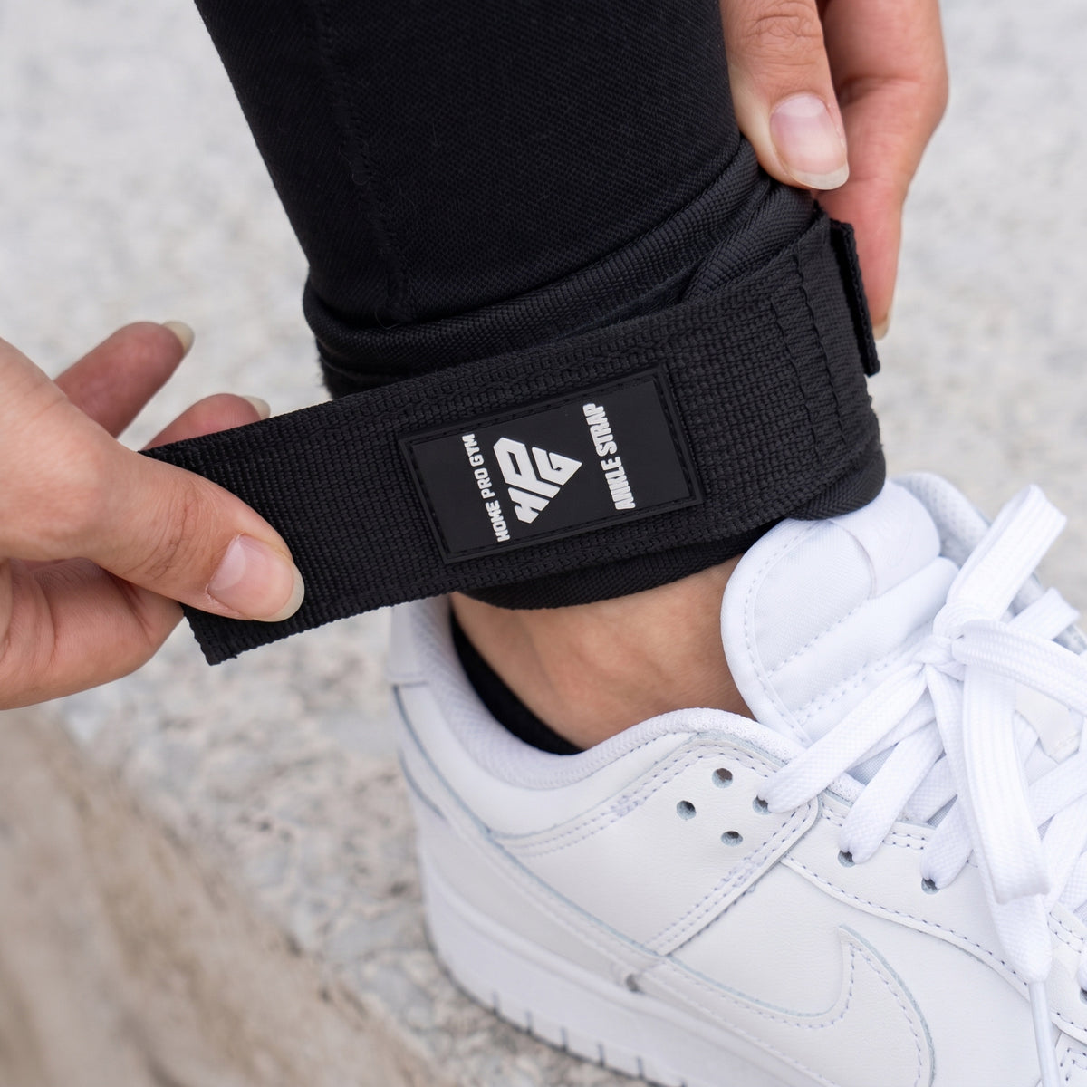 Hands fastening the hook-and-loop closure of an Ankle Strap above a trainer.