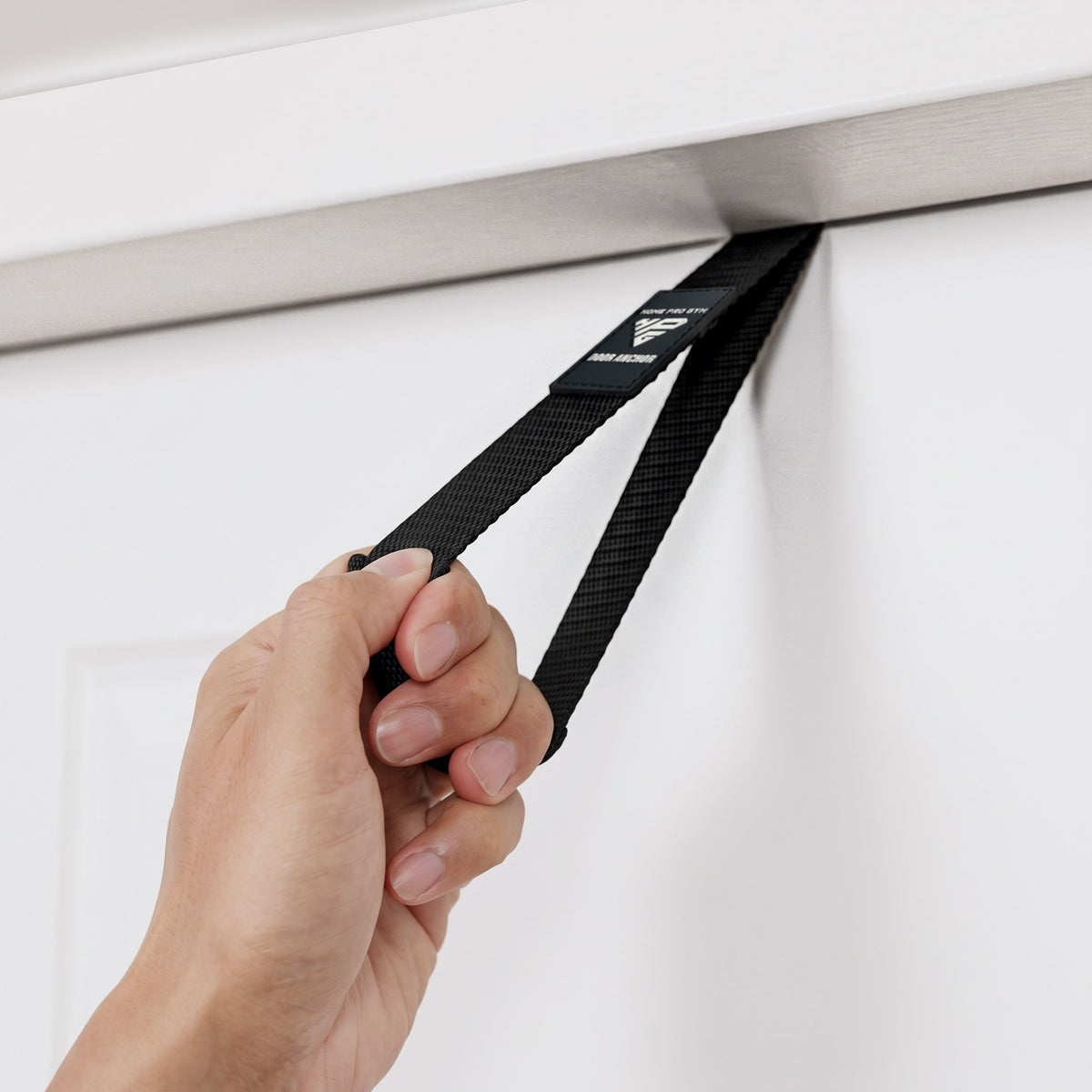 Hand placing the Door Anchor strap over the top edge of a door.
