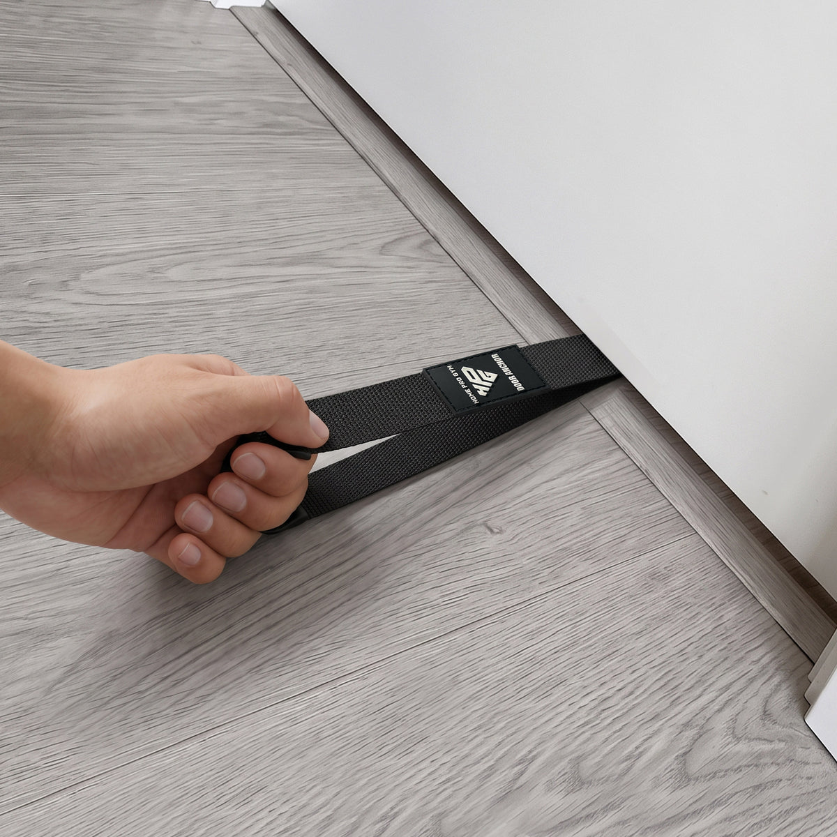 Hand sliding the Door Anchor strap under the bottom of a door.