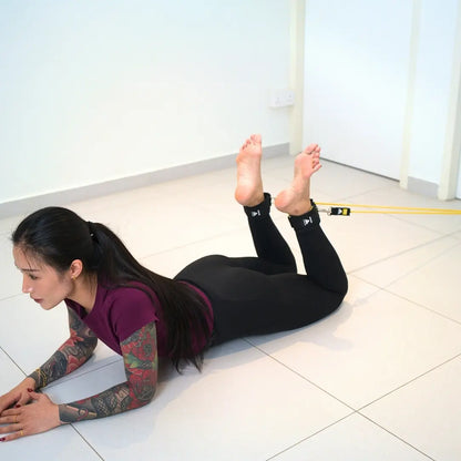 woman performing lying leg curls exercise with HomeProGym PowerTube stackable resistance bands attached via HomeProGym ankle straps at home
